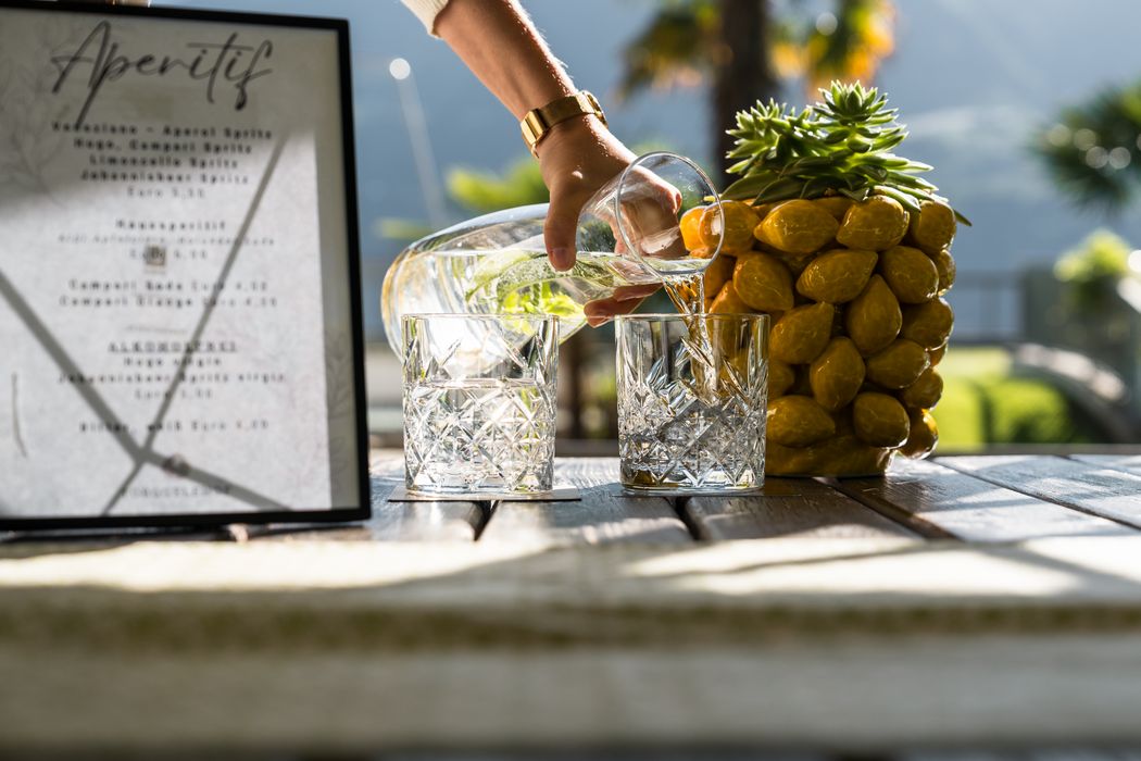 Hand gießt Wasser aus Karaffe in zwei Gläser auf Holztisch mit Dekoration und Aperitif-Menü Hand gießt Wasser aus Karaffe in zwei Gläser auf Holztisch mit Dekoration und Aperitif-Menü
