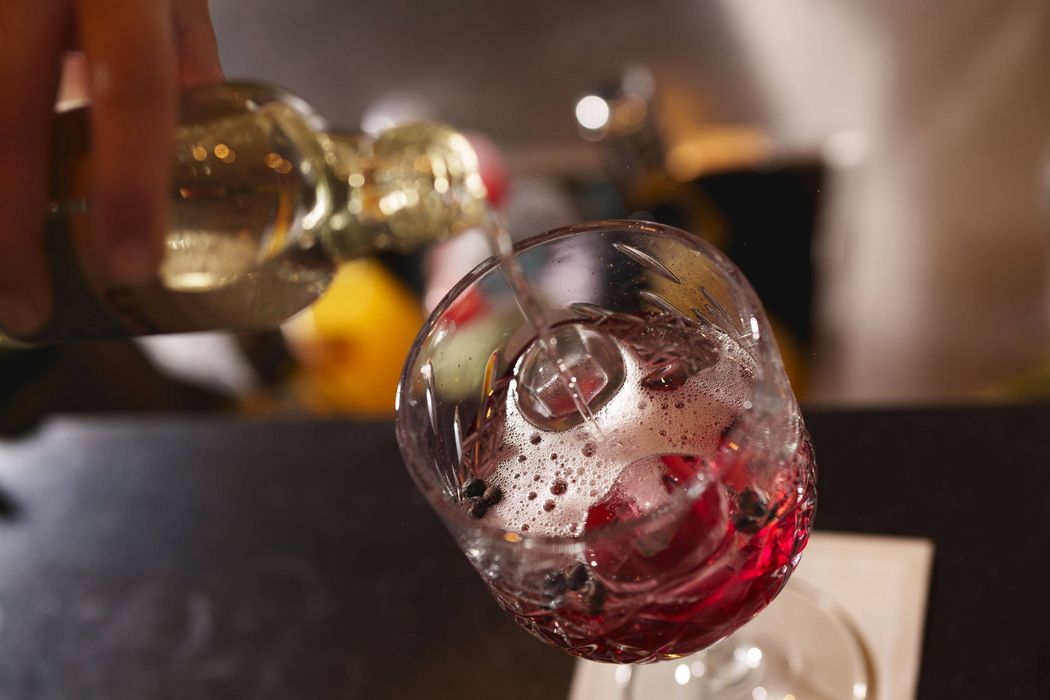 Nahaufnahme eines Glases mit rotem Getränk, Eiswürfeln und Beeren, in das Flüssigkeit eingeschenkt wird. Nahaufnahme eines Glases mit rotem Getränk, Eiswürfeln und Beeren, in das Flüssigkeit eingeschenkt wird.