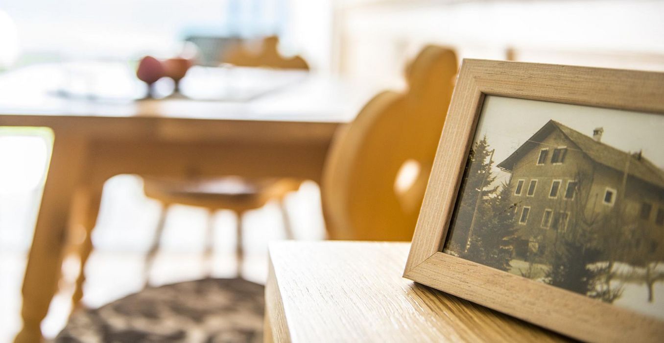 Holzrahmen mit altem Hausfoto auf einem Holztisch, unscharfer Hintergrund mit Holzmöbeln