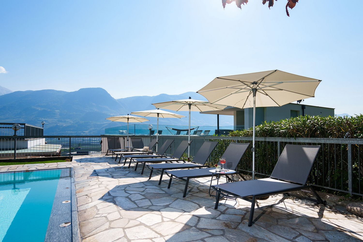 Sonnenliegen mit Sonnenschirmen neben einem Pool auf einer Terrasse mit Bergblick