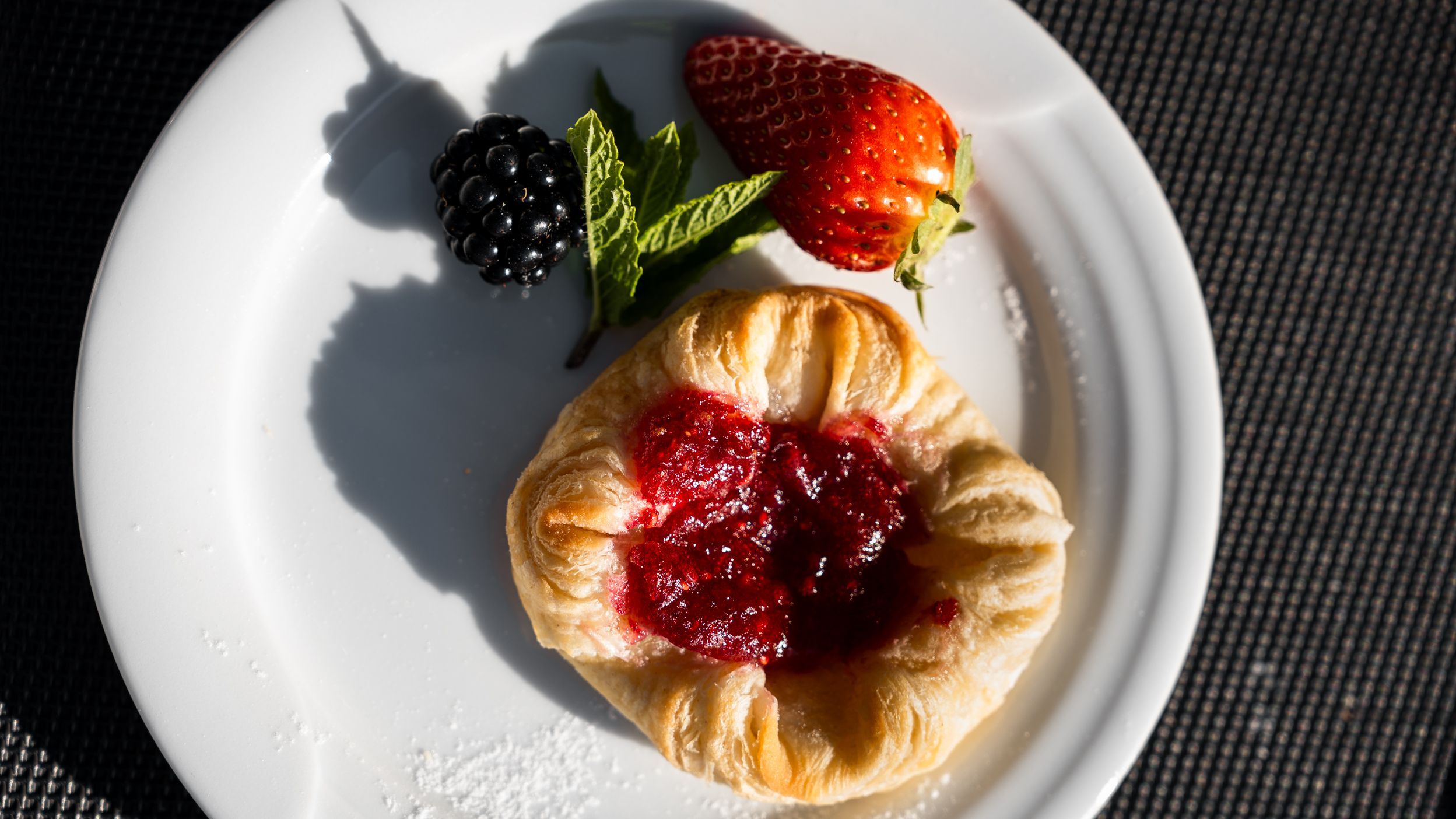 Heller Blätterteigkuchen mit rotem Fruchtbelag auf weißem Teller, daneben eine Brombeere, eine Erdbeere und Minzblätter.