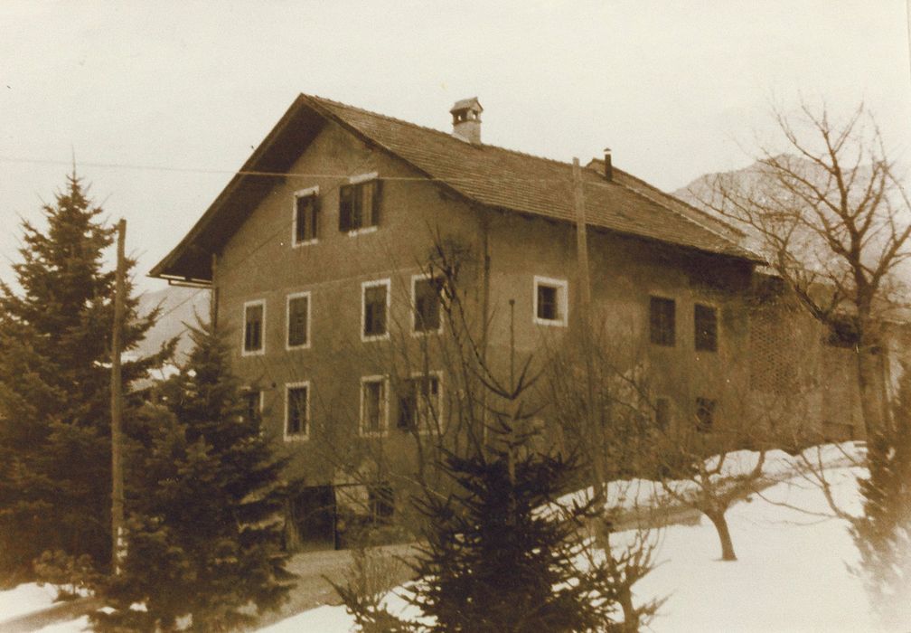 Altes Landhaus mit verschneitem Garten und kahlen Bäumen, umgeben von Tannen.