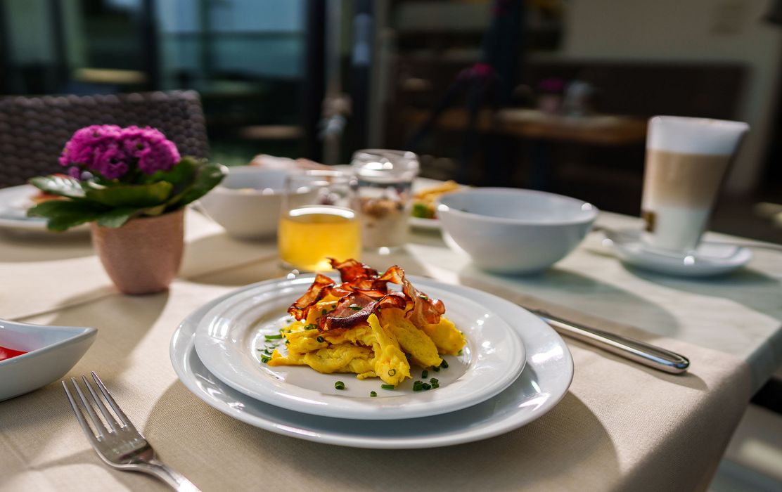 Frühstückstisch mit Rührei und knusprigem Speck auf weißem Teller, dazu Kaffee und Orangensaft Frühstückstisch mit Rührei und knusprigem Speck auf weißem Teller, dazu Kaffee und Orangensaft