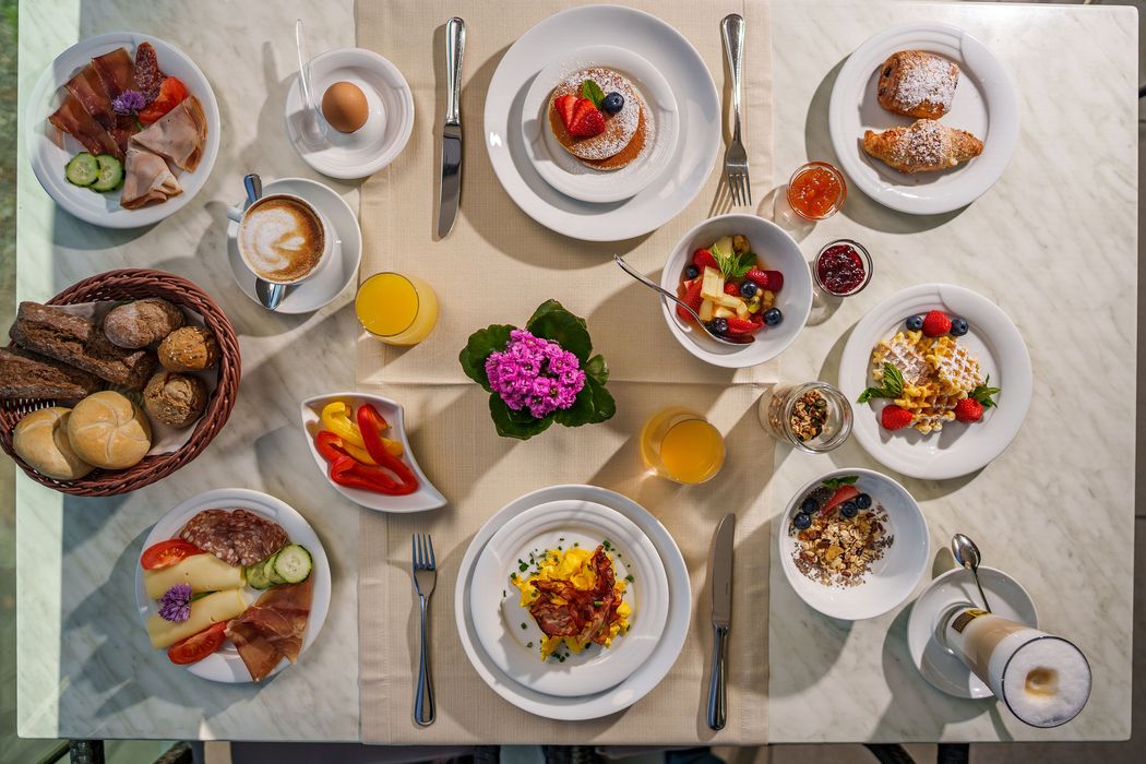 Frühstückstisch mit verschiedenen Speisen wie Brot, Aufschnitt, Eiern, Obst, Pfannkuchen, Waffeln und Getränken. Frühstückstisch mit verschiedenen Speisen wie Brot, Aufschnitt, Eiern, Obst, Pfannkuchen, Waffeln und Getränken.